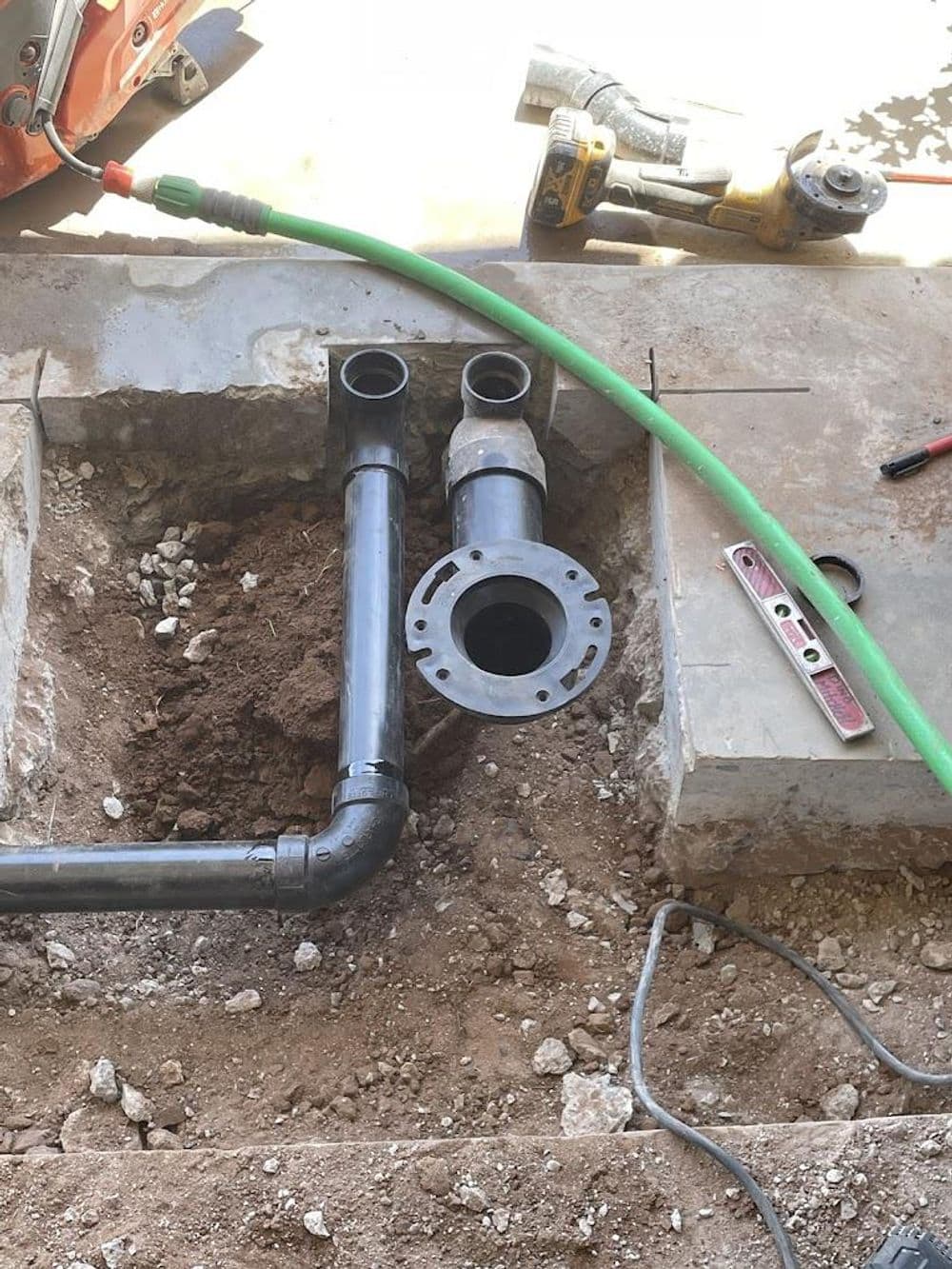 Black PVC pipes installed in ground with tools and equipment for plumbing work visible.