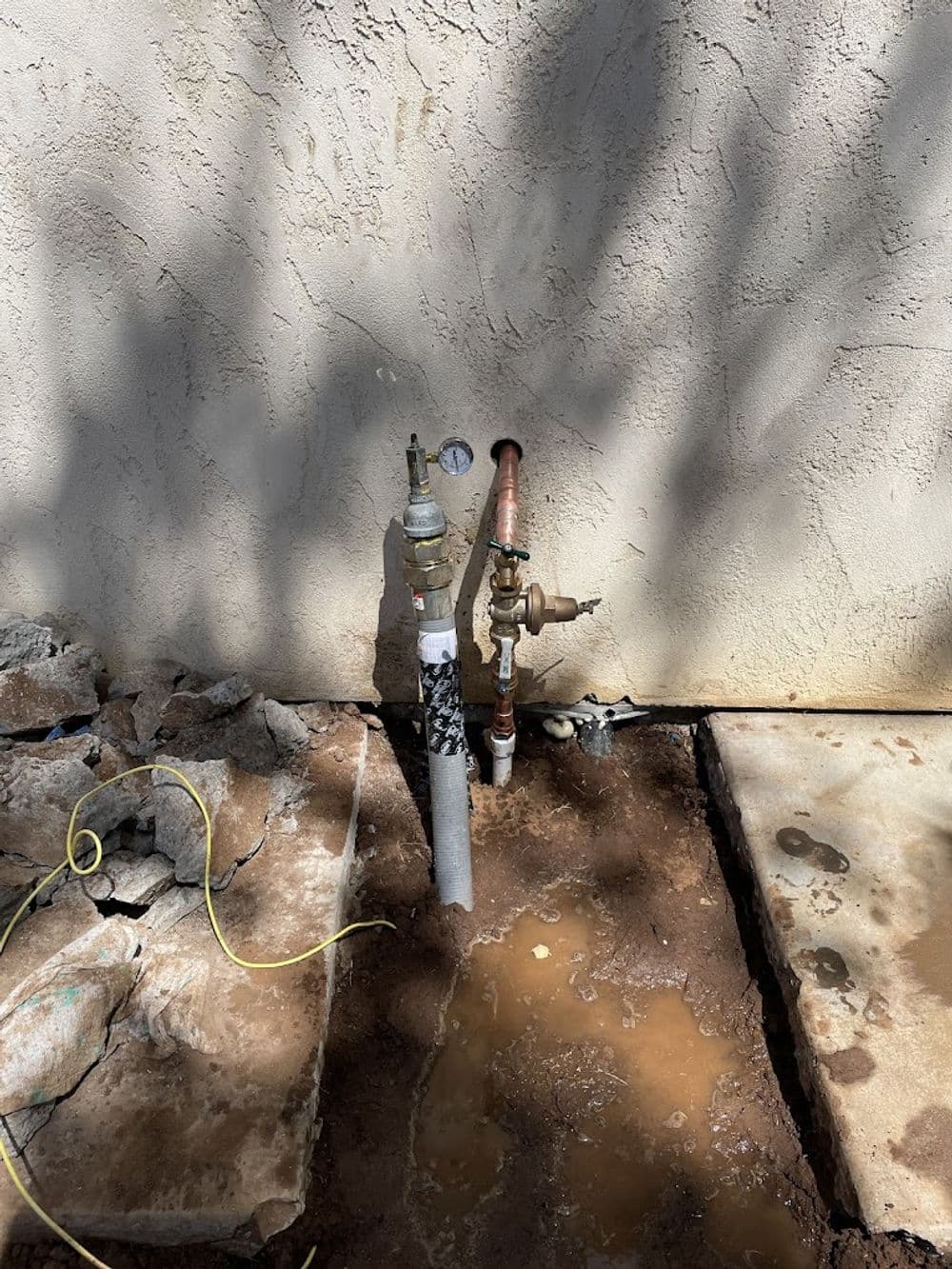 Water pipes and valves next to a wall, with signs of leaking near a foundation.